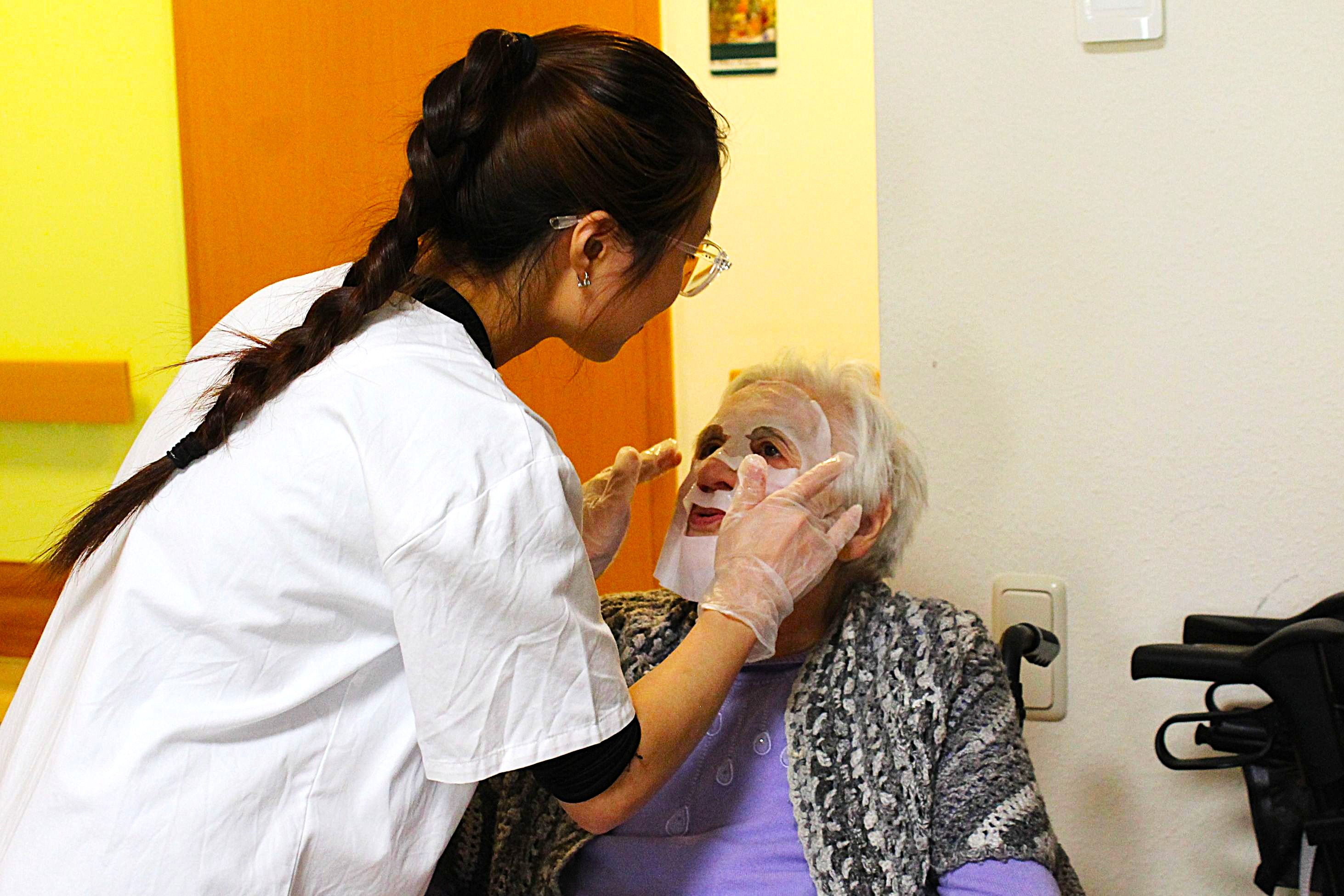 Eine Betreuerin trägt einer Bewohnerin unserer Senioreneinrichtung eine Gesichtsmaske auf.